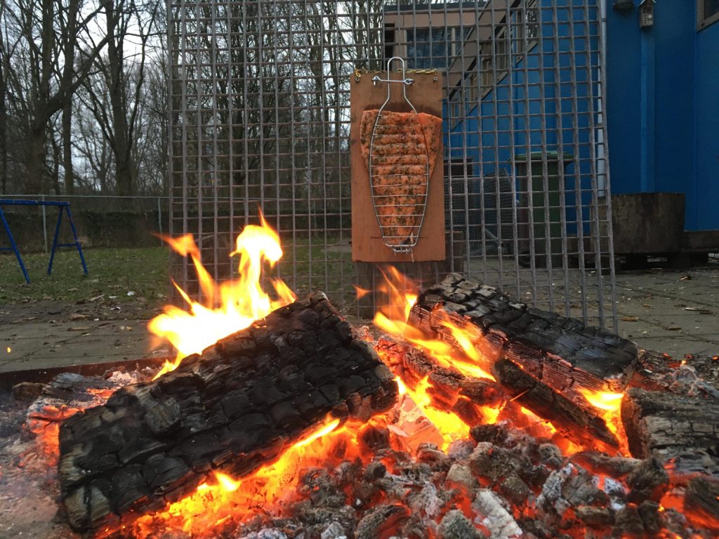 plusscouts bakken zalm op een plank  bij een kampvuur